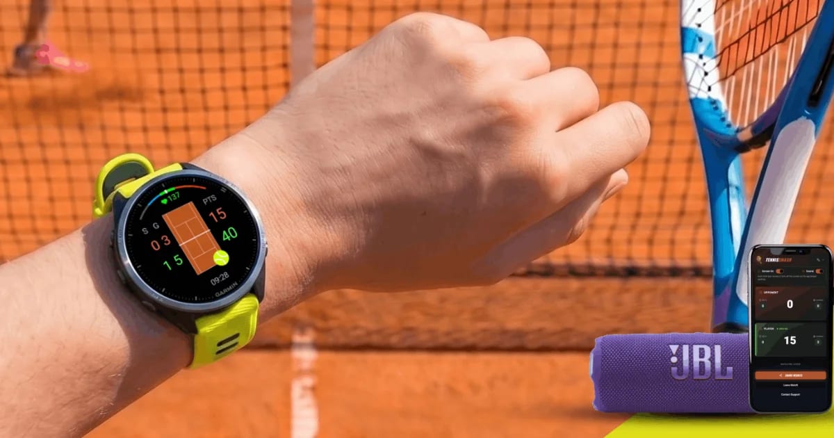 A Garmin watch running Tennis Smash on a player's wrist at a clay court, with a phone showing the live score and a portable Bluetooth speaker